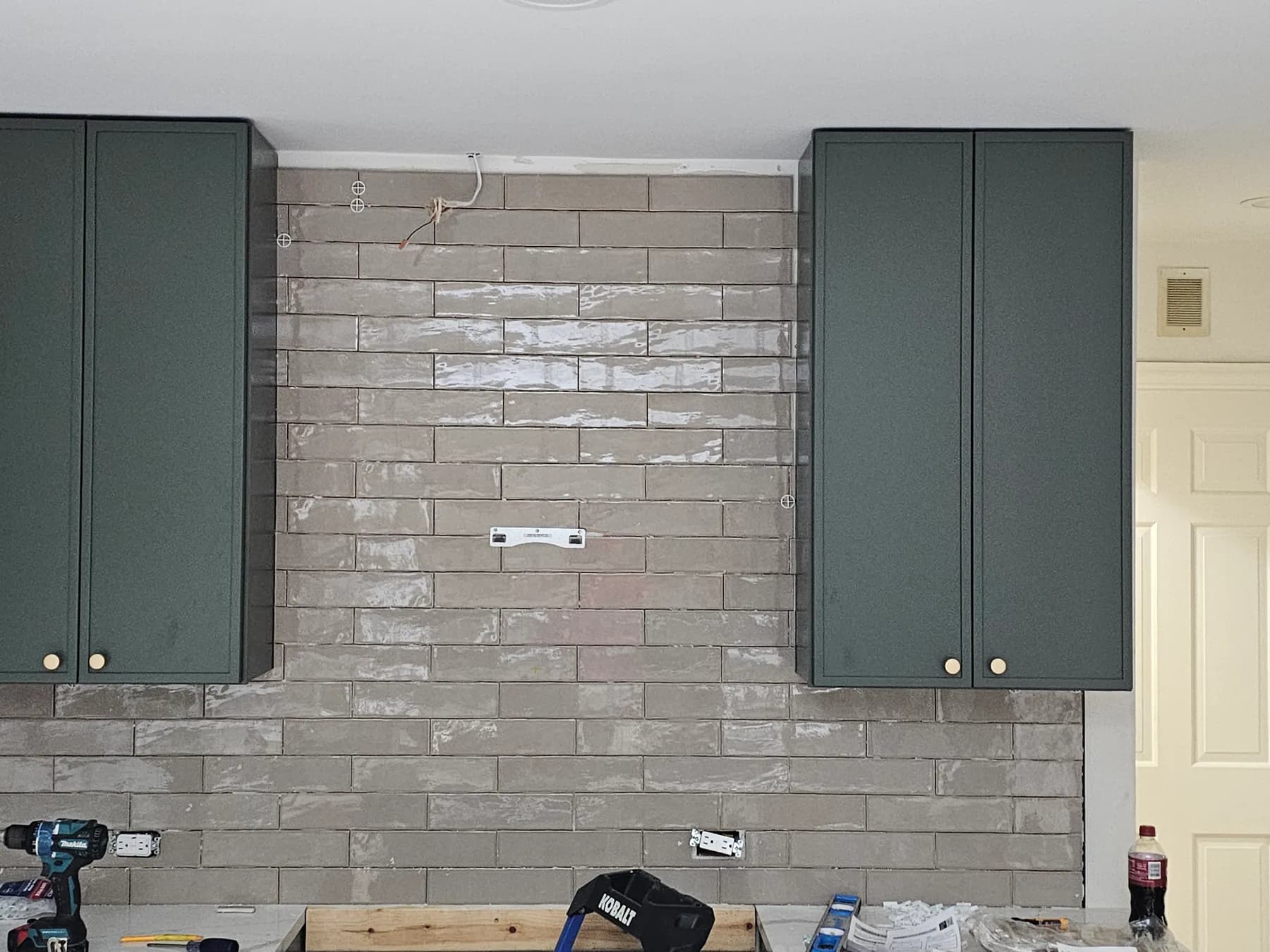 Gray subway tile backsplash being installed between dark kitchen cabinets