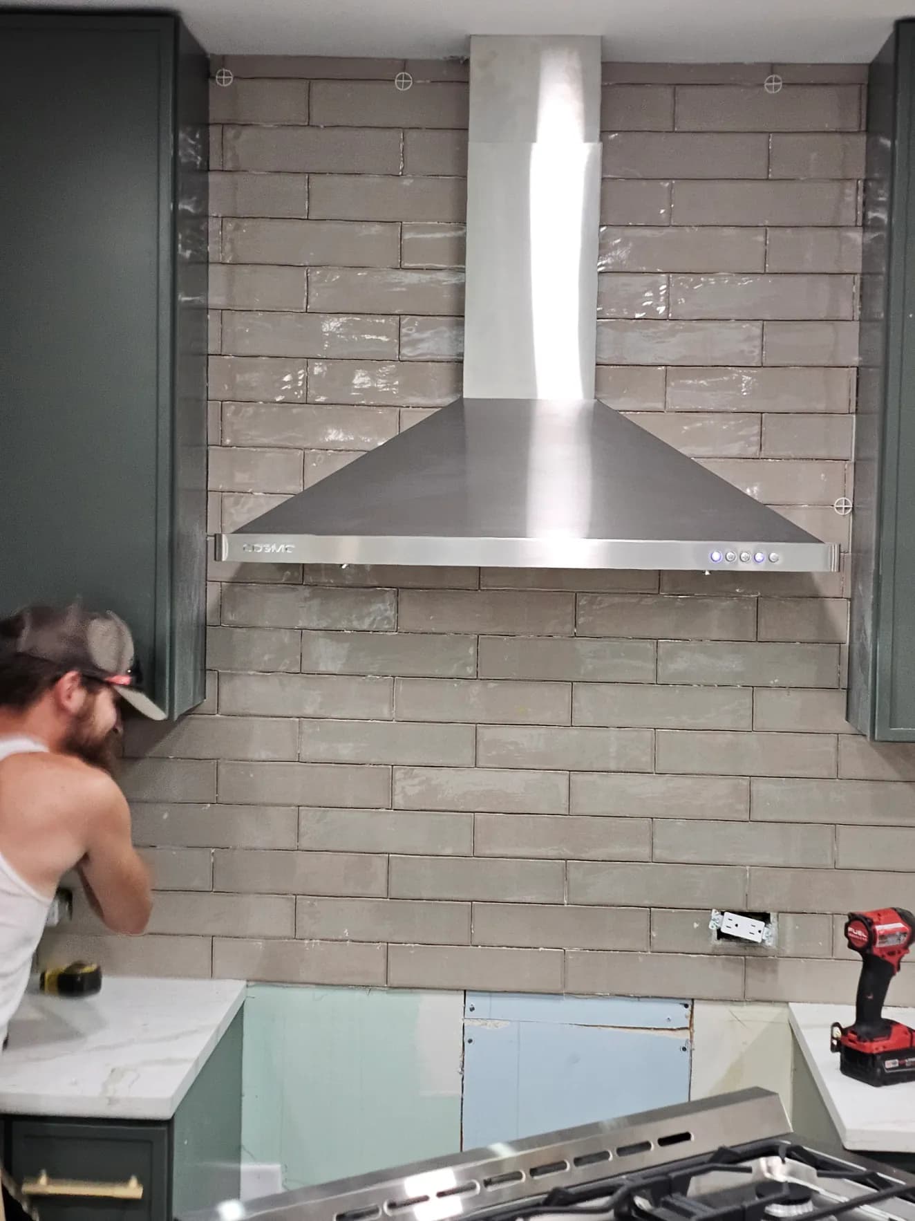 Craftsperson installing gray backsplash tile around a stainless range hood